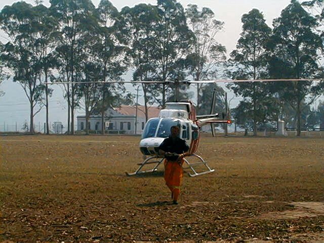 A firefighter walking away from a small helicopter in a smoke-hazed paddock