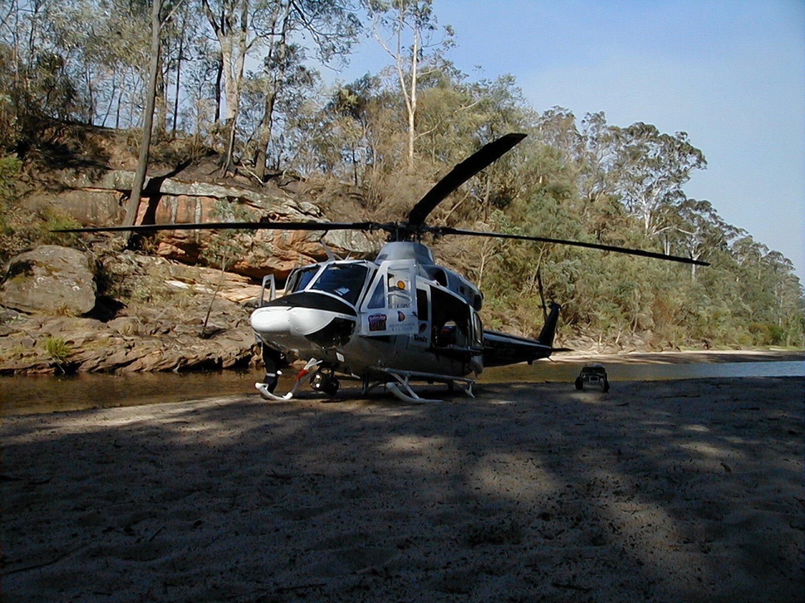 A rescue helicopter parked on a river sandbank below a fire-blackened ridge
